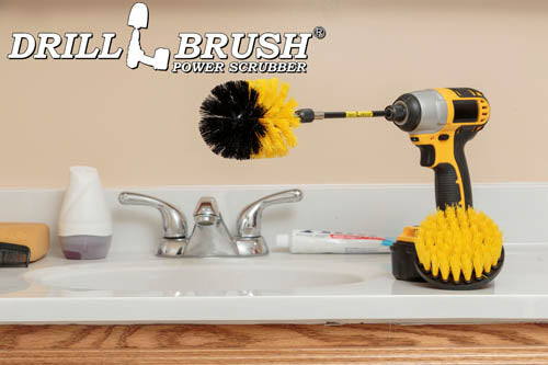 The Drillbrush 4O-5X Medium Yellow Bathroom Brush Kit in a cordless drill sitting on a bathroom counter next to a sink and toiletries.