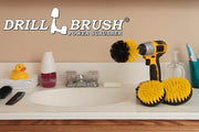 The Drillbrush 54O Medium Yellow Bathroom Brush Kit in a cordless drill sitting on a bathroom counter next to a sink and toiletries.