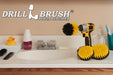 The Drillbrush 54O Medium Yellow Bathroom Brush Kit in a cordless drill sitting on a bathroom counter next to a sink and toiletries.
